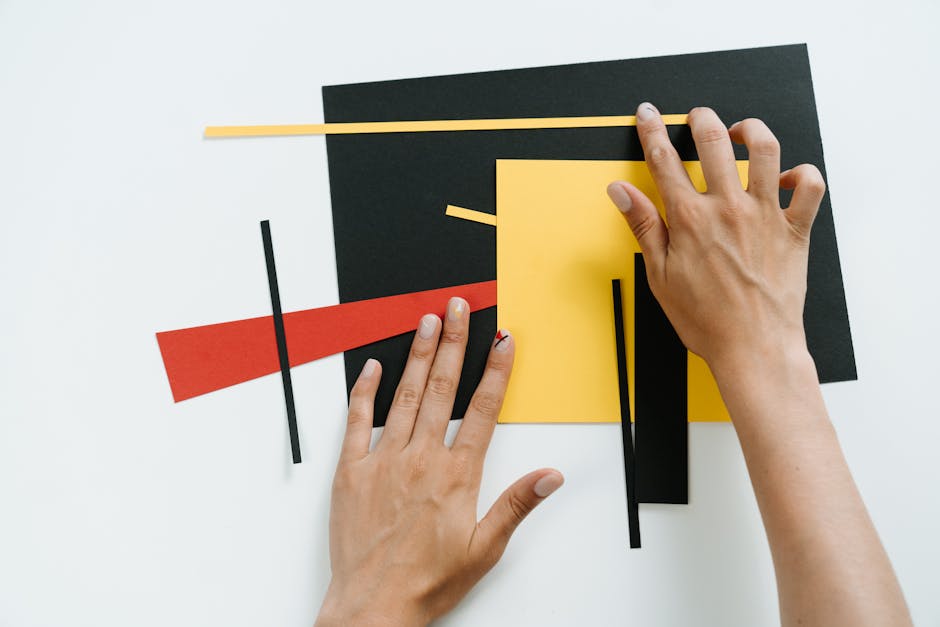 Hands arranging colorful geometric paper shapes in a modern abstract collage.
